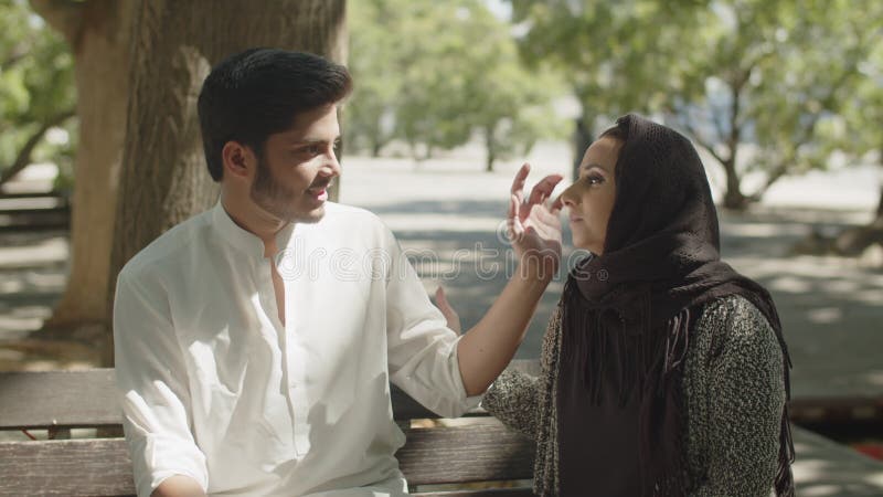 Charmant couple musulman assis sur le banc dans le parc pendant la chaude journée d'été. banque de vidéos