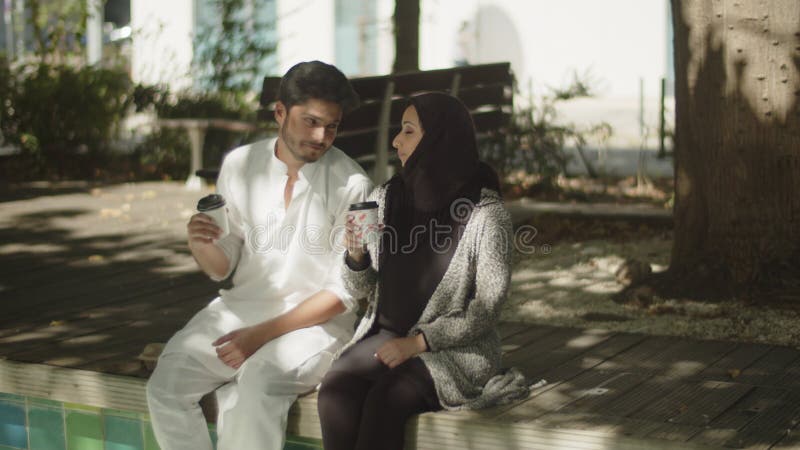 Charmant couple musulman assis sur un banc dans le parc à café. banque de vidéos