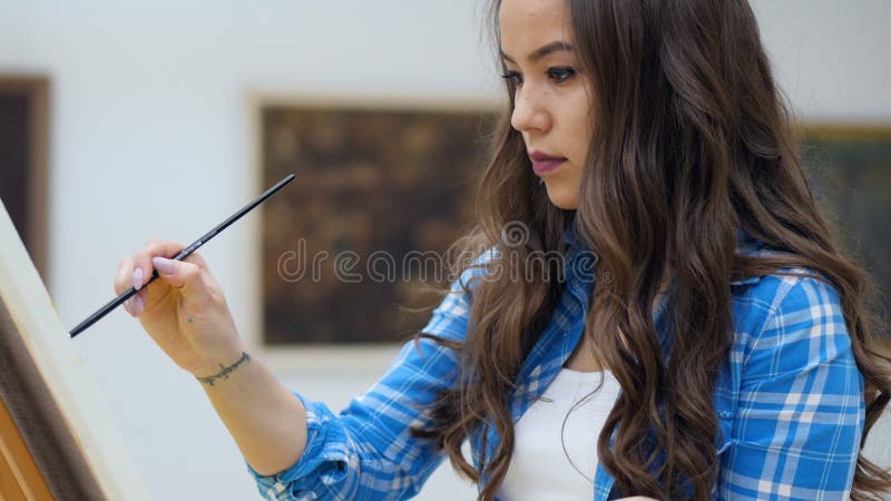 Charming artist girl painting a picture on canvas.