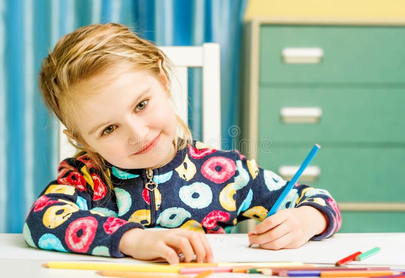 Charming blonde little girl draws with pencils