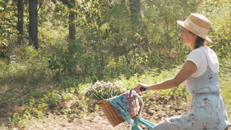 Charming dreamy girl is pedaling on vintage bicycle in summer park. Happy romantic woman rides retro bike in forest at sunny day.