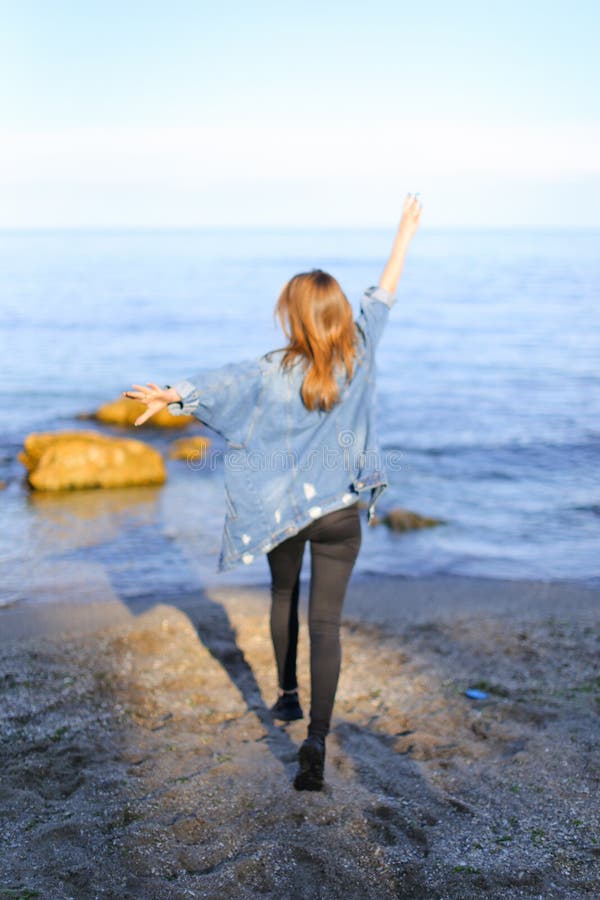 Charming girl walks along coast and merrily fools around on sand