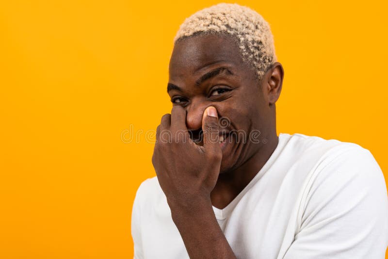 Charming handsome black blond american man laughing while covering his mouth with his hand on an orange background