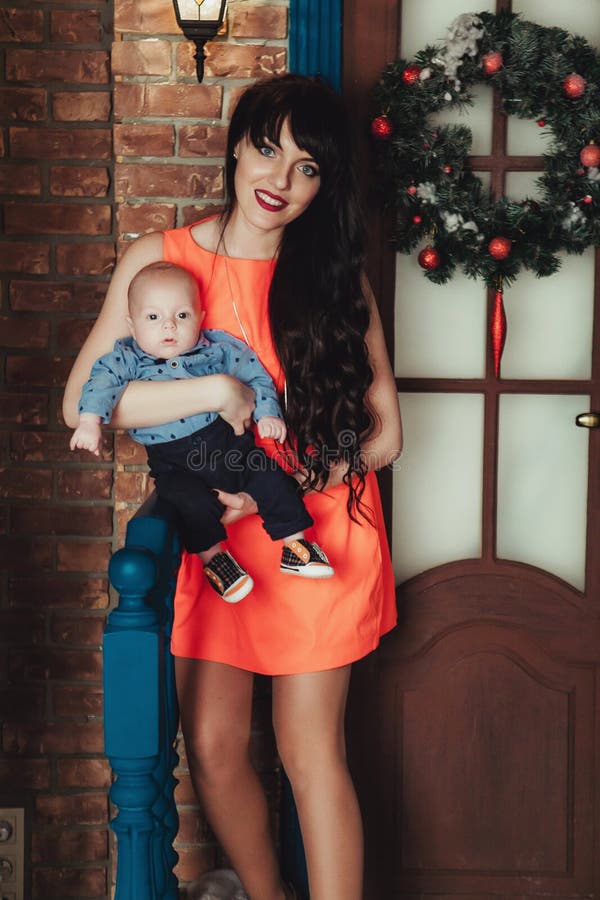 Charming little boy on mother`s hands near door with christmas wreath