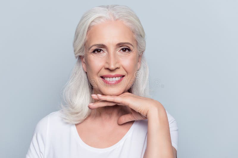 Antico e affascinante donna che tiene una mano sotto il mento con un raggiante sorriso guardando la telecamera su sfondo grigio.