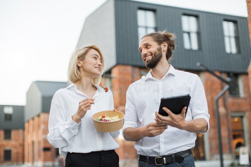 Charming woman holding a cardboard bowl with fresh organic salad and attractive man with tablet.