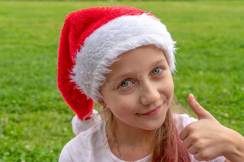 Charming 8 years old girl in santa claus hat raises a finger up and smiles. Christmas. New year concept. copy space. stock images Charming 8 years old girl in santa claus hat raises a finger up and smiles. Christmas. New year concept. copy space. stock images