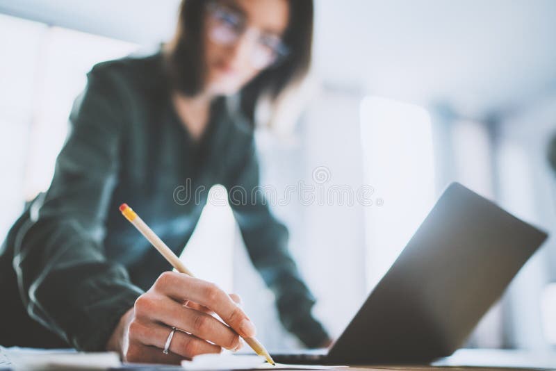 Charming young businesswoman writing something in note pad while working at office.Blurred background