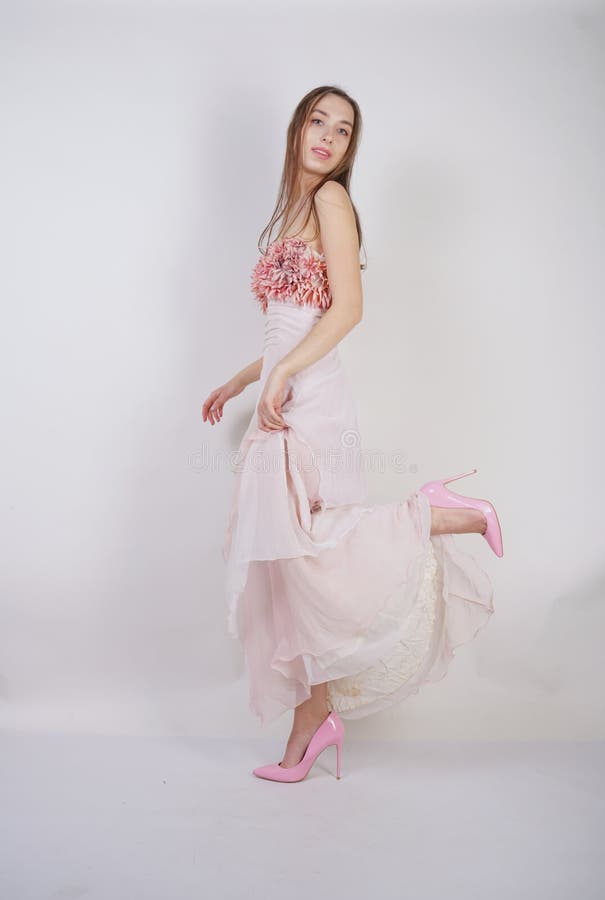 A charming young caucasian girl stands in a pink long prom dress with flower petals on her chest and poses on a white background i royalty free stock images A charming young caucasian girl stands in a pink long prom dress with flower petals on her chest and poses on a white background i royalty free stock images