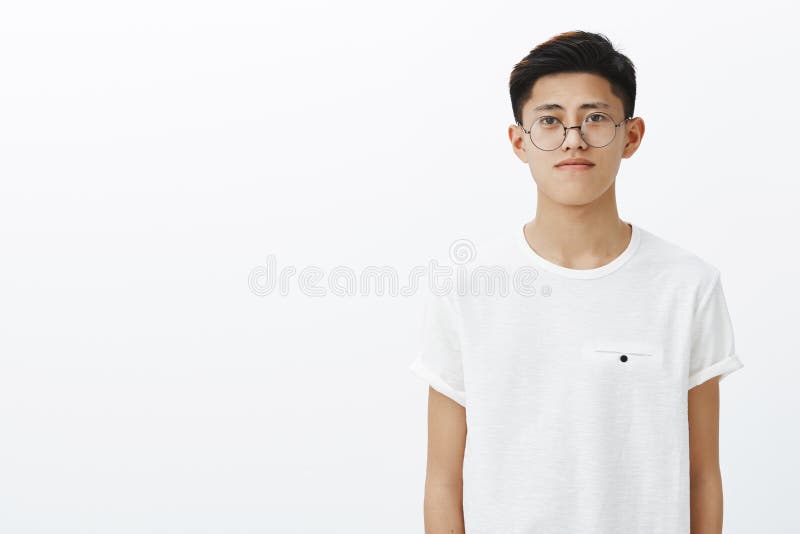 Charming young chinese guy in trendy glasses and t-shirt standing to right side of copy space with friendly expression royalty free stock images Charming young chinese guy in trendy glasses and t-shirt standing to right side of copy space with friendly expression royalty free stock images