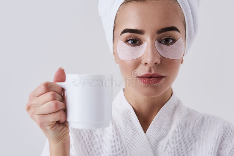 Charming young lady with patches under eyes holding cup of coffee