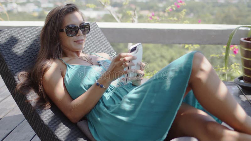 Attractive woman with smartphone resting on chaise lounge