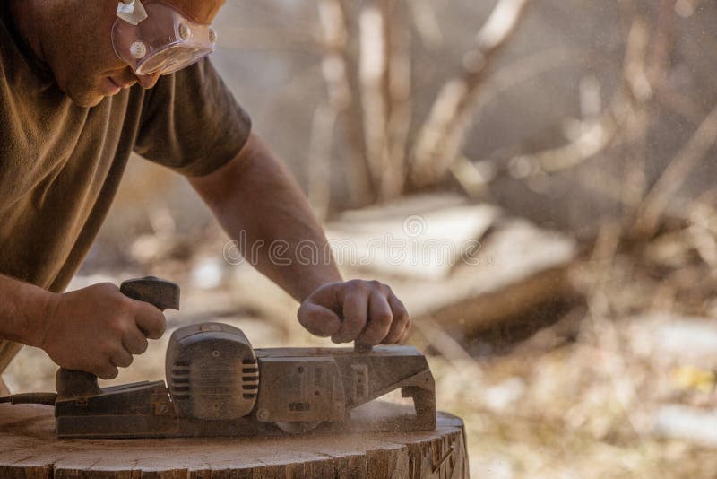 Charpentier travaillant avec la planeuse électrique sur le tronçon en bois en plein air photos stock Charpentier travaillant avec la planeuse électrique sur le tronçon en bois en plein air photos stock
