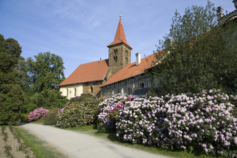Pruhonice Chateau with blooming rhododendrons along a garden path.