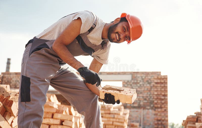 Che presentano e tengono in mano una piccola pala e un mattone. il bel indiano è sul cantiere immagine stock libera da diritti