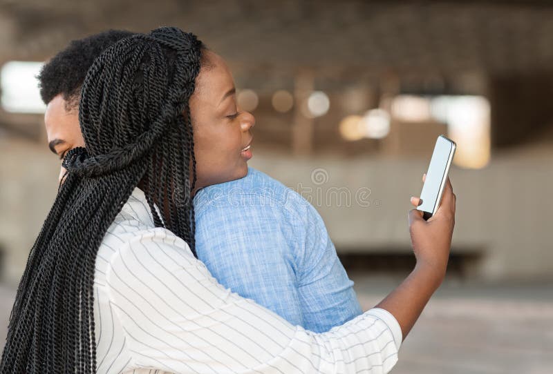 Cheating wife. Black women texting on cellphone with somebody while hugging with her boyfriend outdoors, copy space. Cheating wife. Black women texting on cellphone with somebody while hugging with her boyfriend outdoors, copy space