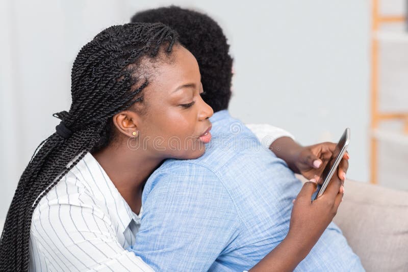 Cheating wife. Young black women texting on cellphone with somebody while embracing her husband at home, closeup. Cheating wife. Young black women texting on cellphone with somebody while embracing her husband at home, closeup