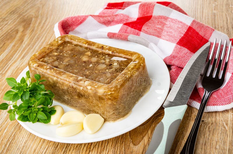 Napkin, piece of meat jelly, basil, garlic in white plate, knife and fork on wooden table stock photography Napkin, piece of meat jelly, basil, garlic in white plate, knife and fork on wooden table stock photography