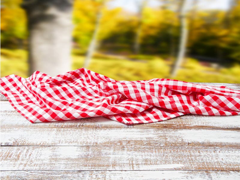 Checkered tablecloth on old wooden table on blurred park background, holiday concept stock images Checkered tablecloth on old wooden table on blurred park background, holiday concept stock images