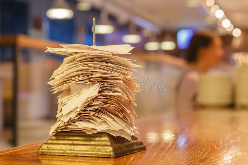 Checks from completed orders in the bar or restaurant kitchen impaled on a sharp thin iron needle on stand. Concept checker, stan stock photos Checks from completed orders in the bar or restaurant kitchen impaled on a sharp thin iron needle on stand. Concept checker, stan stock photos