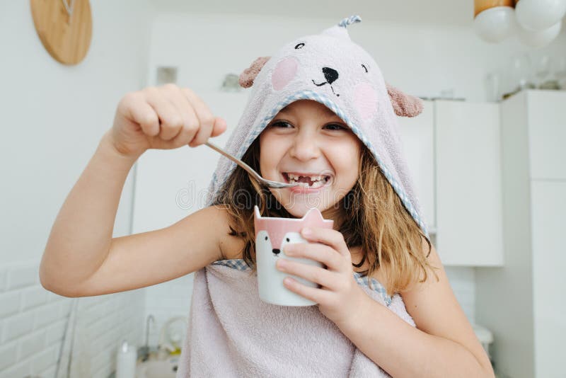 Cheeky little girl wrapped in a bear hooded towel, eating yogurt from a cup