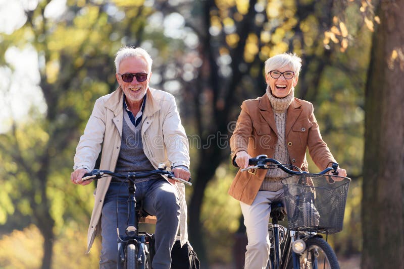 Cheerful active senior couple with bicycles in the public park together having fun. Perfect activities for elderly people.