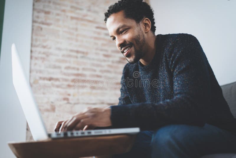 Cheerful African man using computer and smiling while sitting on the sofa. Concept of young business people working at stock photo