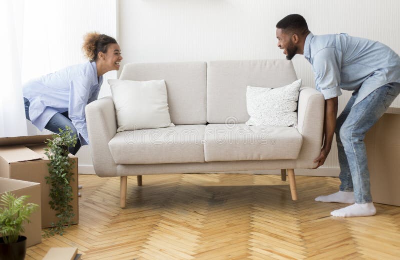 Cheerful Afro Spouses Placing Couch Furnishing Empty Room In New House royalty free stock photos Cheerful Afro Spouses Placing Couch Furnishing Empty Room In New House royalty free stock photos