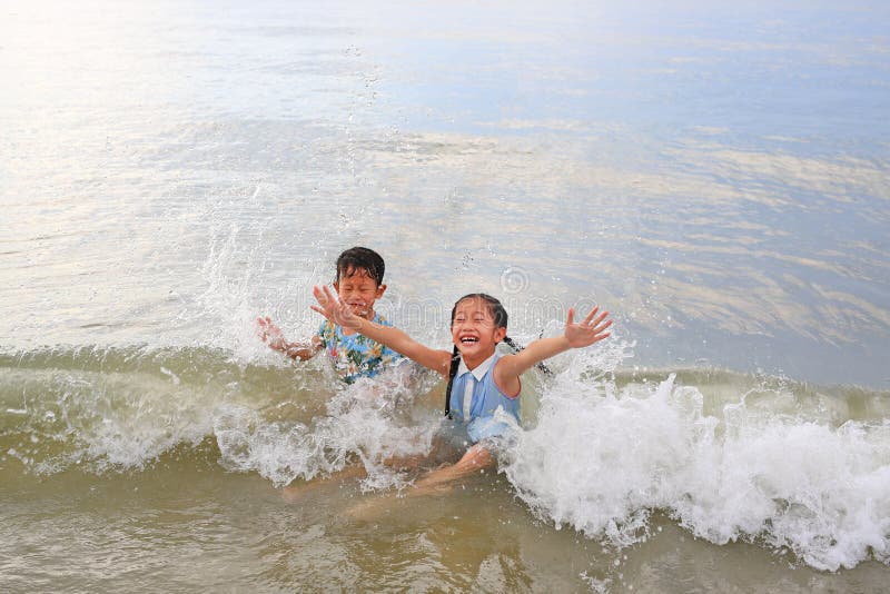 Cheerful Asian little boy and young girl child enjoy playing and lying on tropical sea beach at sunrise. Adorable sister and