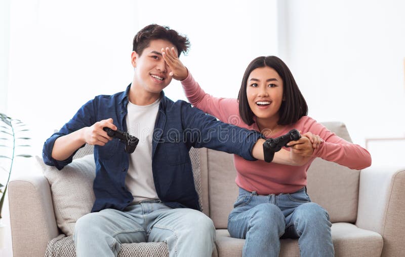 Happy Asian Couple Playing Computer Video Game Sitting On Couch At