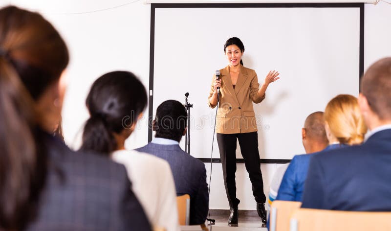 Cheerful asian woman business coach leading discussion with audience stock image