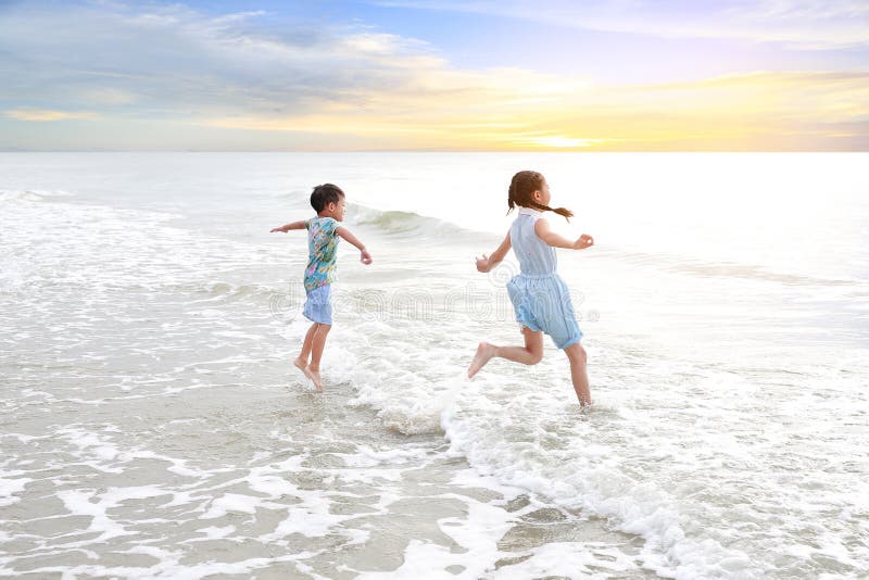 Cheerful Asian young sister and little brother having fun together on tropical sand beach at sunrise. Happy family boy and girl