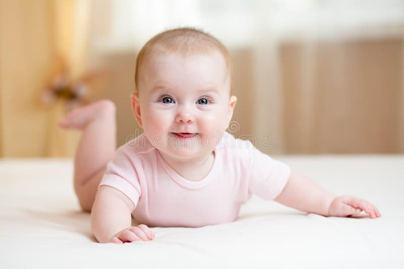 Cheerful baby girl lying on white bed