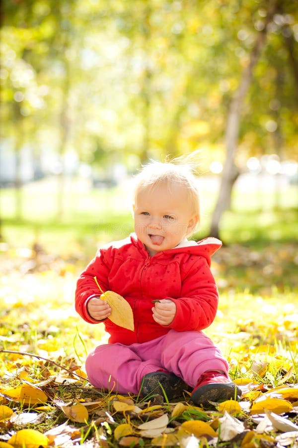 Cheerful baby play with yellow leafs in park