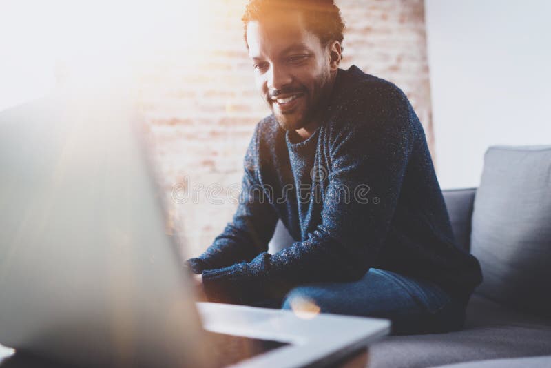 Cheerful bearded African man working on laptop while sitting sofa at his modern office place.Concept of young people royalty free stock photography Cheerful bearded African man working on laptop while sitting sofa at his modern office place.Concept of young people royalty free stock photography