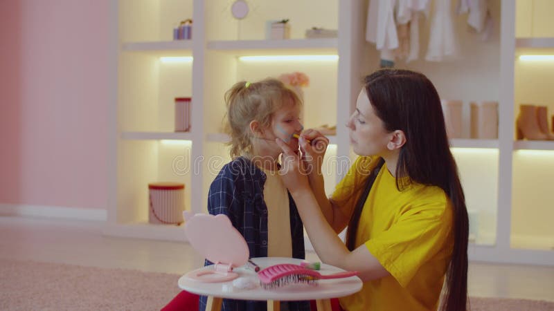 Cheerful lovely mother painting adorable preschool age girl as cat