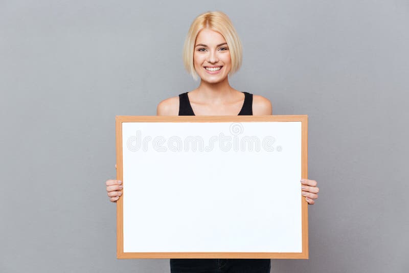 Cheerful beautiful young woman holding blank white board. 