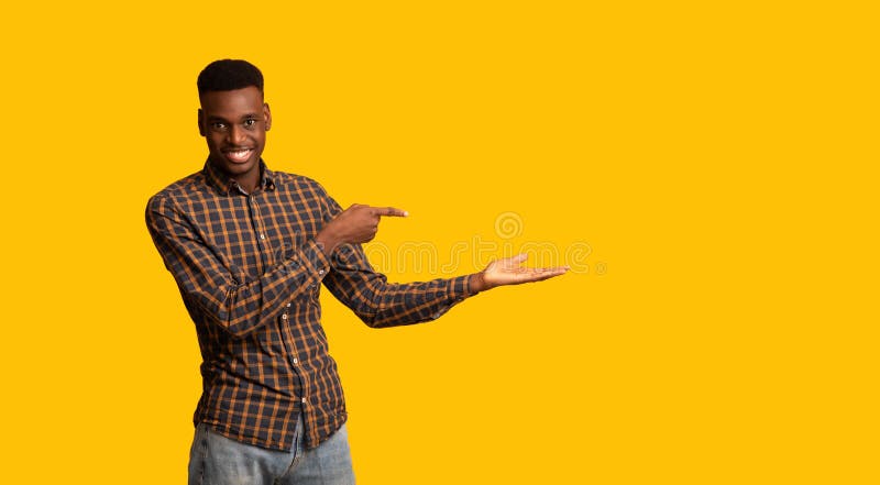 Cheerful Black Guy Pointing Finger At Open Palm, Isolated On Yellow Background