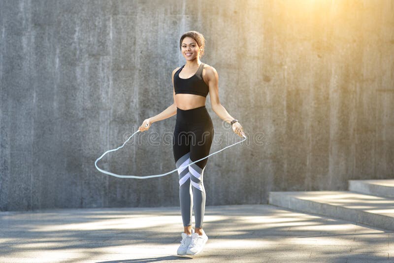 Cheerful black sporty girl jumping with skipping rope at park, exercising outdoor, copy space, sun flare. Cheerful black sporty girl jumping with skipping rope at park, exercising outdoor, copy space, sun flare