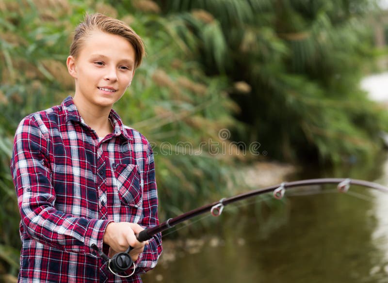 Cheerful boy casting line for fishing on lake