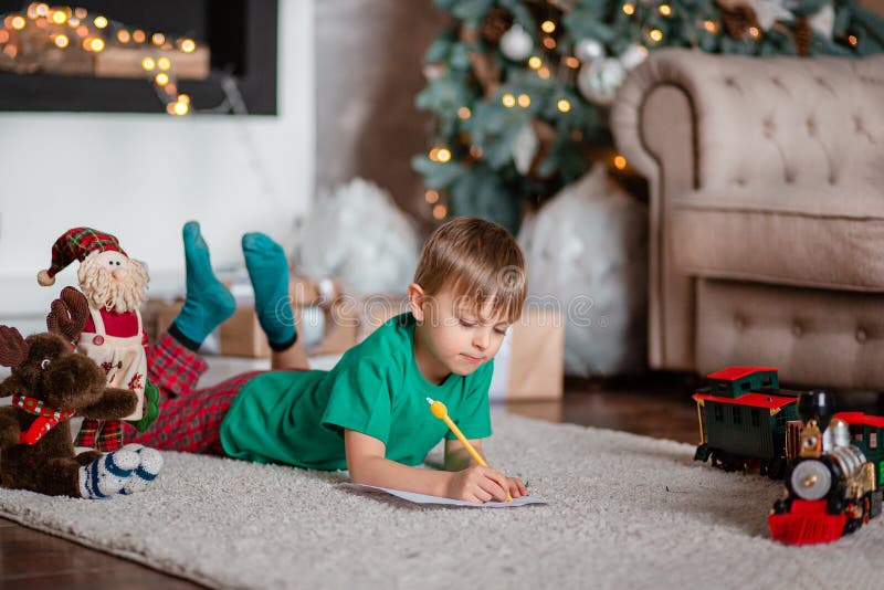 Cheerful boy is a letter to Santa, near the Christmas tree. Happy childhood, time for fulfilling wishes