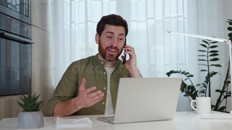 Cheerful Caucasian Man Answering Phone Call while Working at Laptop at