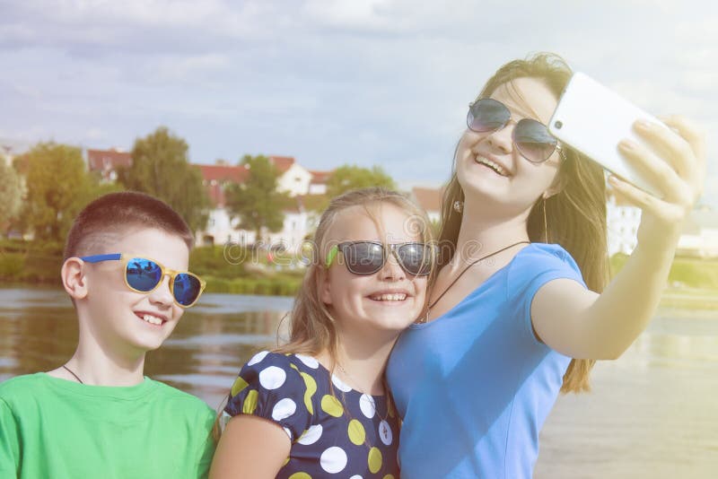 Cheerful children`s company makes selfie on a smartphone on a city street outdoor. stock photo Cheerful children`s company makes selfie on a smartphone on a city street outdoor. stock photo