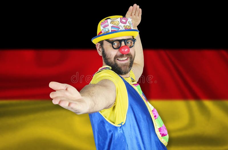 A cheerful clown stands in a welcoming pose against the background of the flag of Germany stock photography