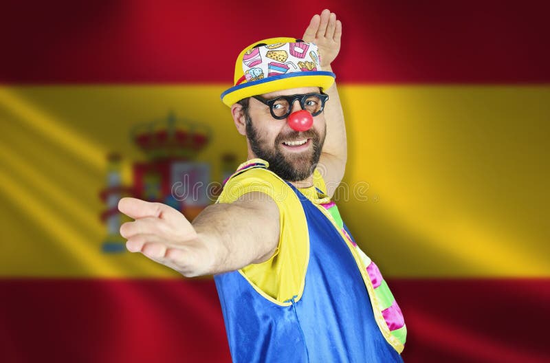A cheerful clown stands in a welcoming pose against the background of the flag of Spain stock image
