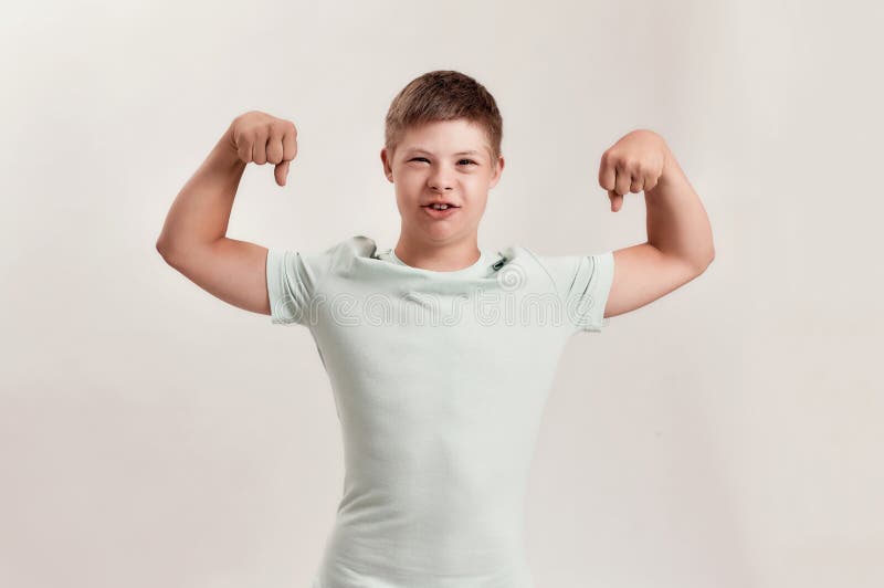 Cheerful disabled boy with Down syndrome looking at camera, raising his arms, showing his strength while standing