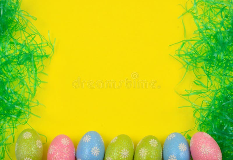 A cheerful Easter background border with sparky, decorative pink, blue and green eggs and plastic Easter grass with a bright