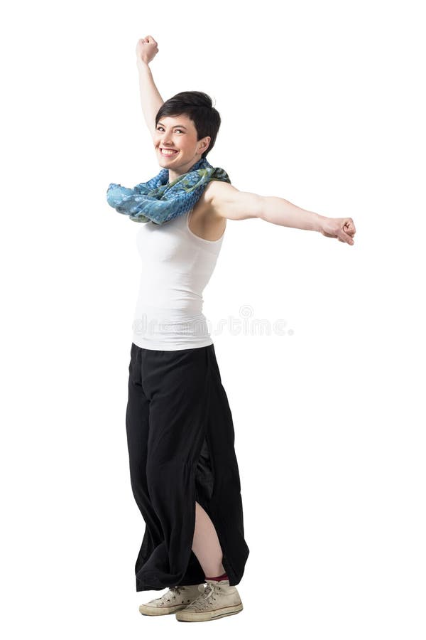 Cheerful excited woman spinning with raised arms wearing wide pants and scarf.