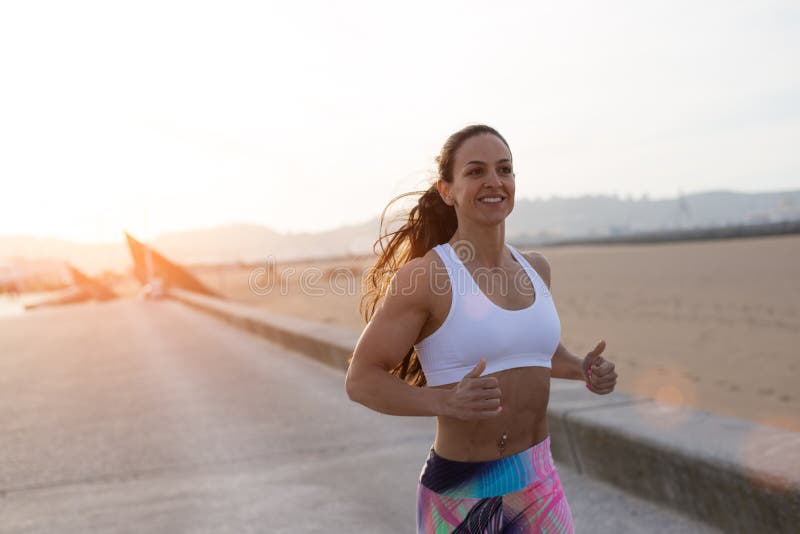 Fitness strong woman running at the beach. Fit female athlete exercising on summer sunset. Gijon, Spain. Fitness strong woman running at the beach. Fit female athlete exercising on summer sunset. Gijon, Spain.