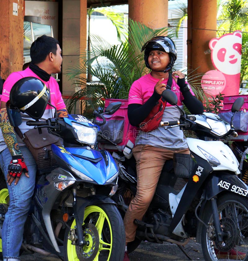 Two cheerful Foodpanda riders on their motorbikes having a chat in Ipoh, Malaysia. Two cheerful Foodpanda riders on their motorbikes having a chat in Ipoh, Malaysia